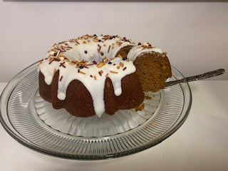 A whole spiced pumpkin bundt cake, generously topped with a thick drizzle of icing and sprinkled with chopped nuts, displayed on a cake stand.