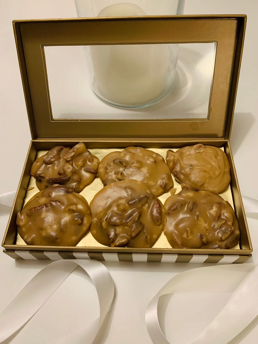 Round, rustic pecan pralines with a glossy, caramel-brown surface, studded with whole pecan halves and set on parchment paper.
